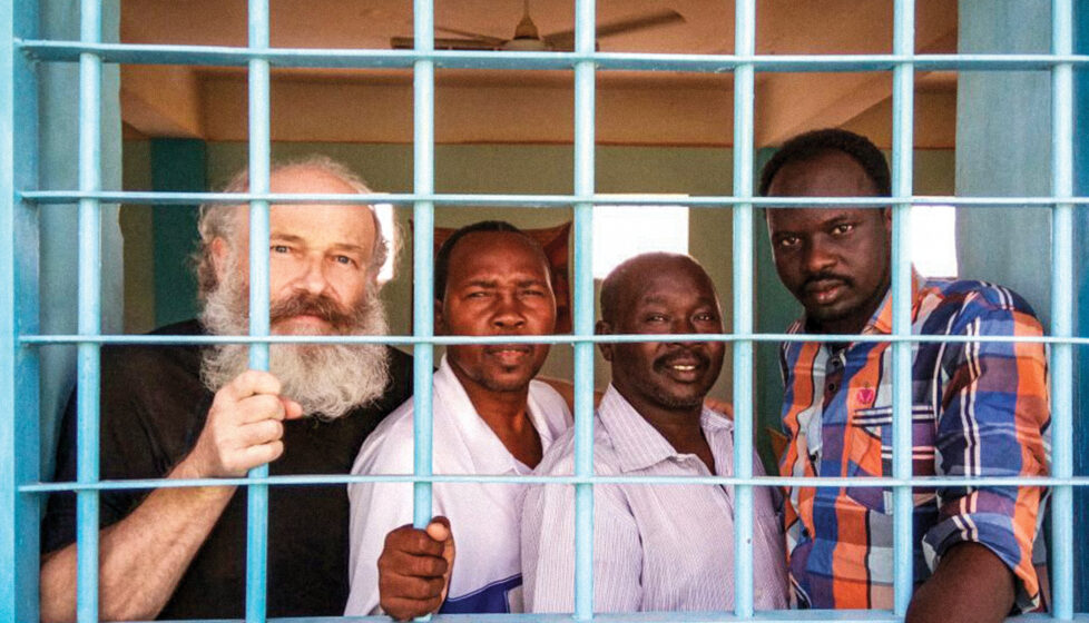 four men stand behind bars in a jail cell