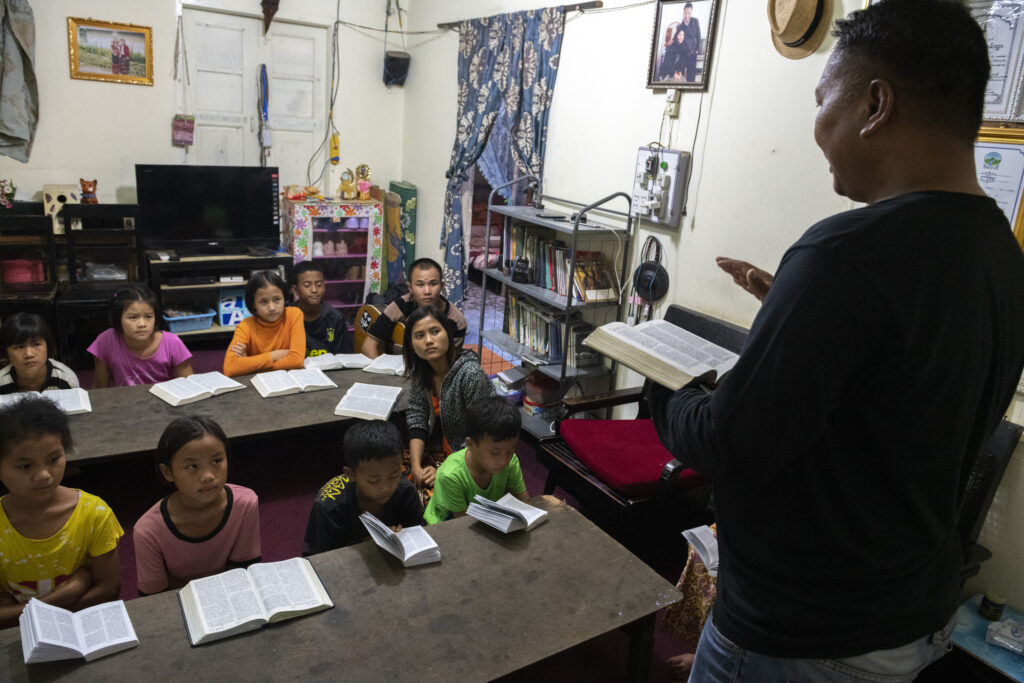 Kan teaches a room full of children at tables from the Bible.